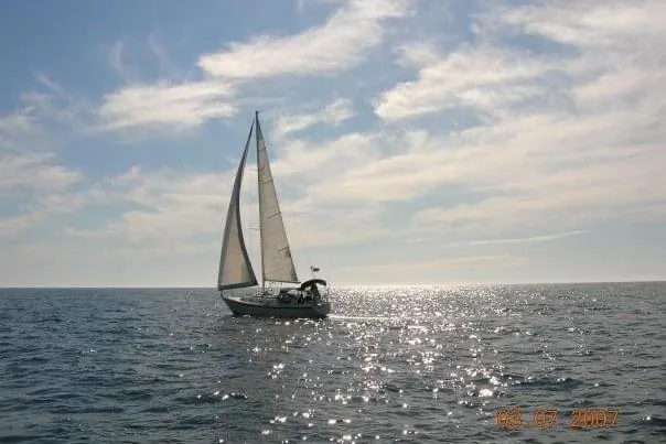 Slide: The Image of Sailboat Ericson 34 (1990) gliding on sparkling ocean under a partly cloudy sky. - 23
