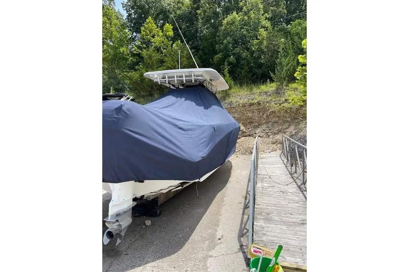 Slide: The Image of 2008 Boston Whaler 320 Outrage covered, parked near a wooden dock, surrounded by trees. - 25