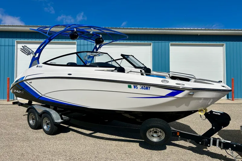 Slide: The Image of 2018 Yamaha Boats 242X on trailer, parked near blue building under clear sky. - 0