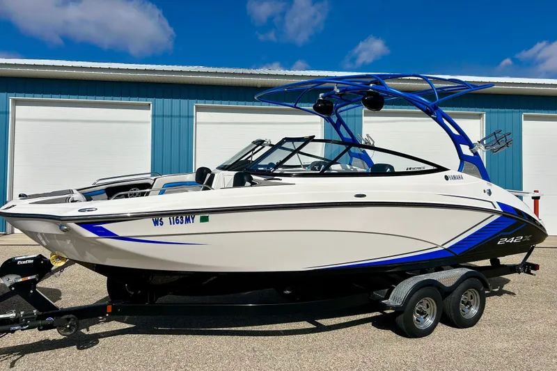 Slide: The Image of 2018 Yamaha Boats 242X on trailer, parked near blue building under clear sky. - 1