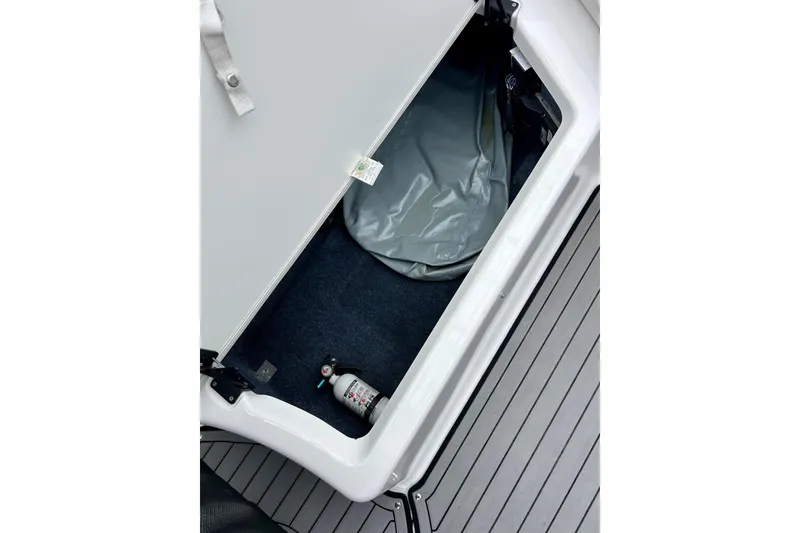 Slide: The Image of Open storage compartment on 2018 Yamaha Boats 242X, featuring a fire extinguisher and gray cover. - 54