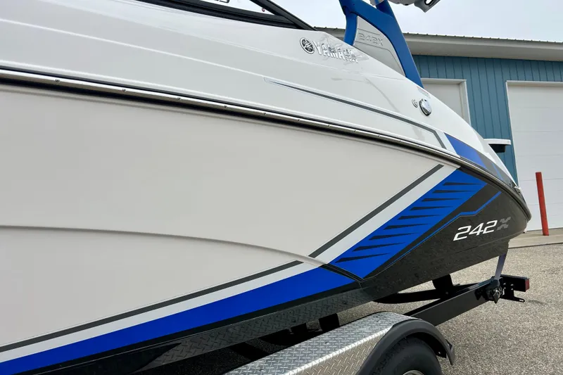 Slide: The Image of 2018 Yamaha Boats 242X, sleek design with blue accents, on trailer near a building. - 61
