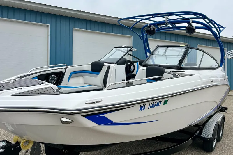 Slide: The Image of 2018 Yamaha Boats 242X, sleek white design, blue accents, parked near blue building. - 73