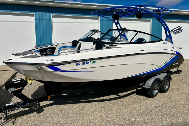 Slide: The Image of 2018 Yamaha Boats 242X on trailer, white and blue, parked outside a blue building. - 75