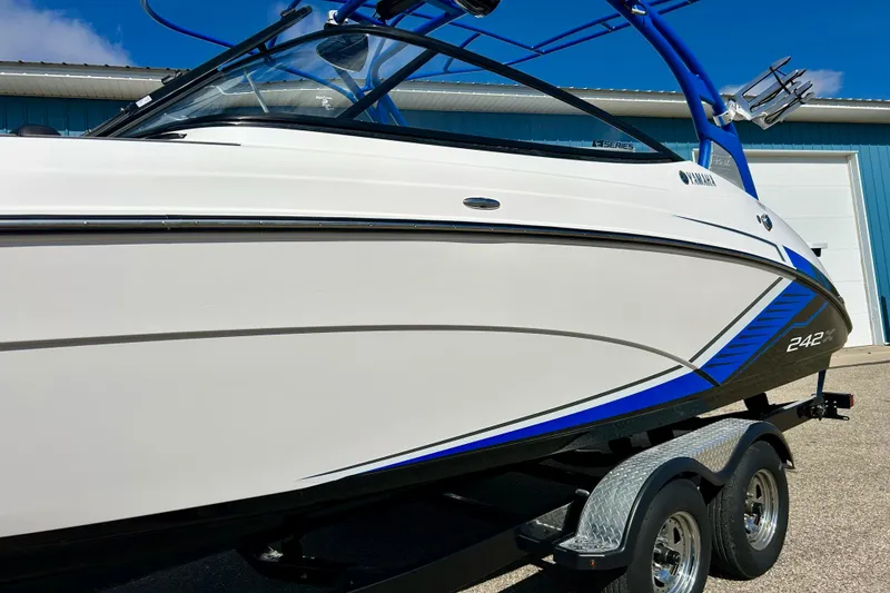 Slide: The Image of 2018 Yamaha Boats 242X, sleek white and blue design, on a trailer outside a building. - 76