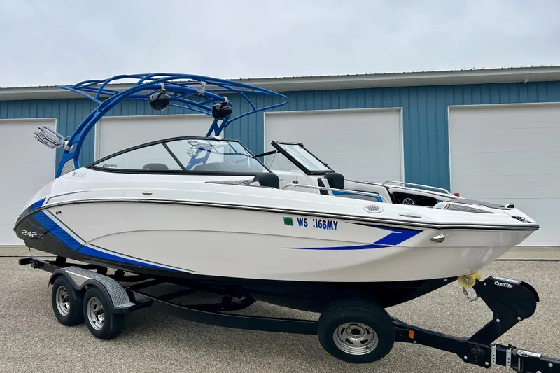 Slide: The Image of 2018 Yamaha Boats 242X on trailer, white with blue accents, parked near garage. - 77