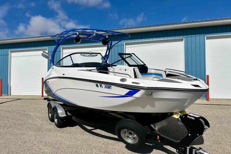 Slide: The Image of 2018 Yamaha Boats 242X on trailer, parked outside blue building under clear sky. - 78