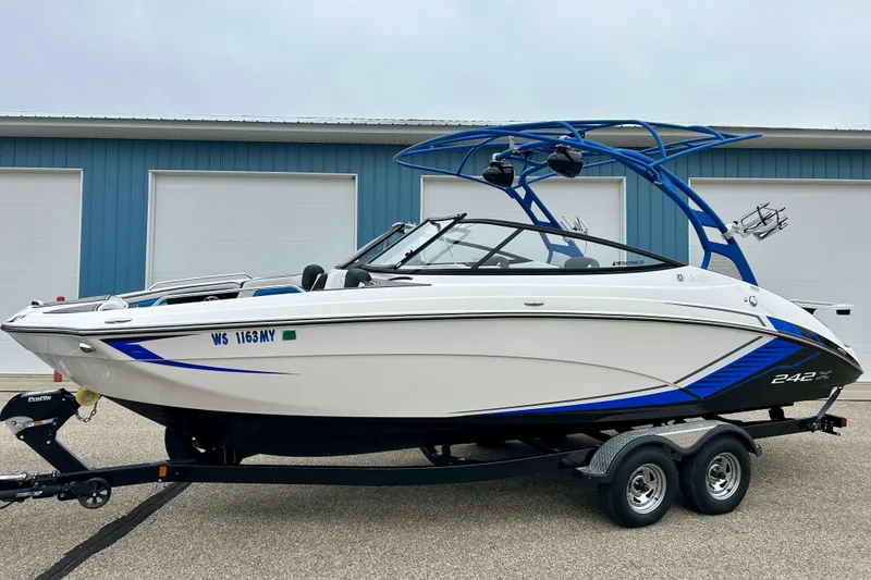 Slide: The Image of 2018 Yamaha Boats 242X on trailer, white and blue design, parked near blue building. - 79