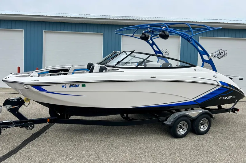 Slide: The Image of 2018 Yamaha Boats 242X on trailer, white and blue, parked near blue building. - 81