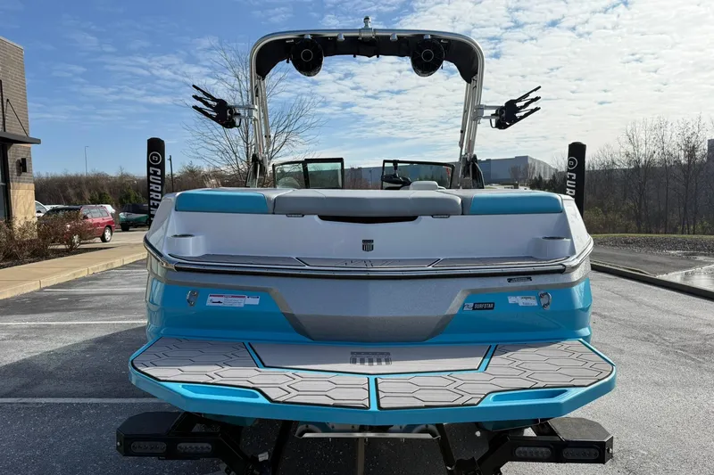 Slide: The Image of 2023 MasterCraft NXT23 boat, rear view, blue and white design, parked outdoors. - 3