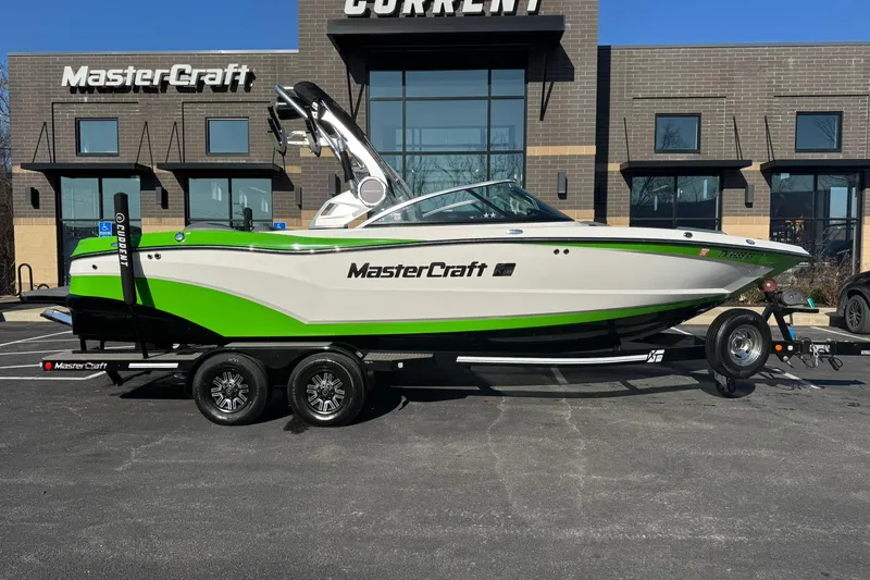 Slide: The Image of 2019 MasterCraft XT23 boat with green accents on a trailer, parked outside a building. - 3