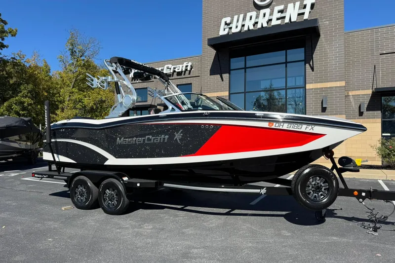 The Image of 2016 MasterCraft X23 boat on trailer, parked outside dealership, featuring sleek black and red design. - 1