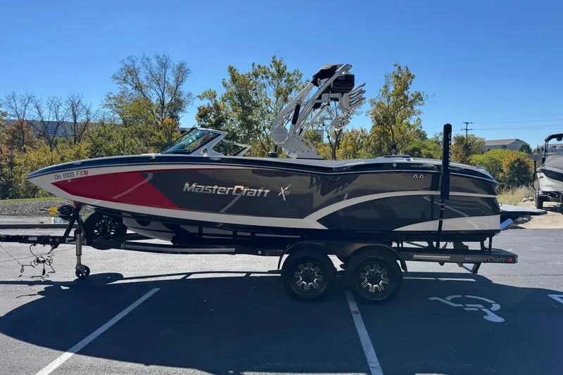 Slide: The Image of 2016 MasterCraft X23 boat on trailer in parking lot, surrounded by trees. - 6