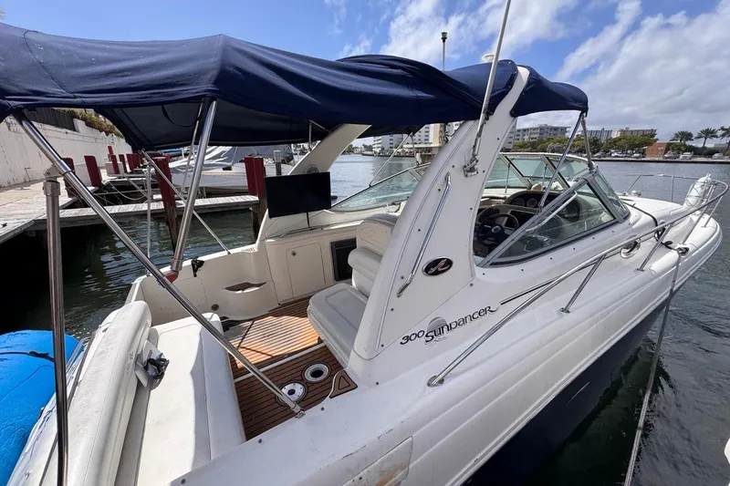 Slide: The Image of 2005 Sea Ray 300 Sundancer boat docked, featuring a blue canopy and spacious seating area. - 10