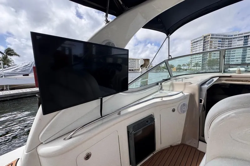Slide: The Image of 2005 Sea Ray 300 Sundancer interior with mounted TV, docked near waterfront buildings. - 18