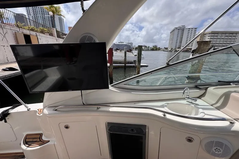 Slide: The Image of 2005 Sea Ray 300 Sundancer boat interior with TV and sink, docked by waterfront buildings. - 27