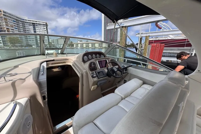Slide: The Image of 2005 Sea Ray 300 Sundancer boat interior with helm, docked near waterfront buildings. - 28