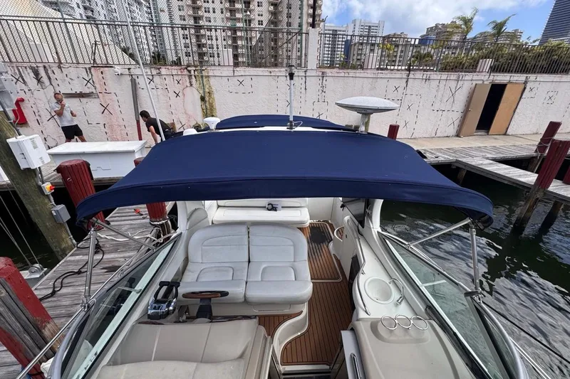 Slide: The Image of 2005 Sea Ray 300 Sundancer docked, featuring blue canopy and white seating, urban backdrop. - 49