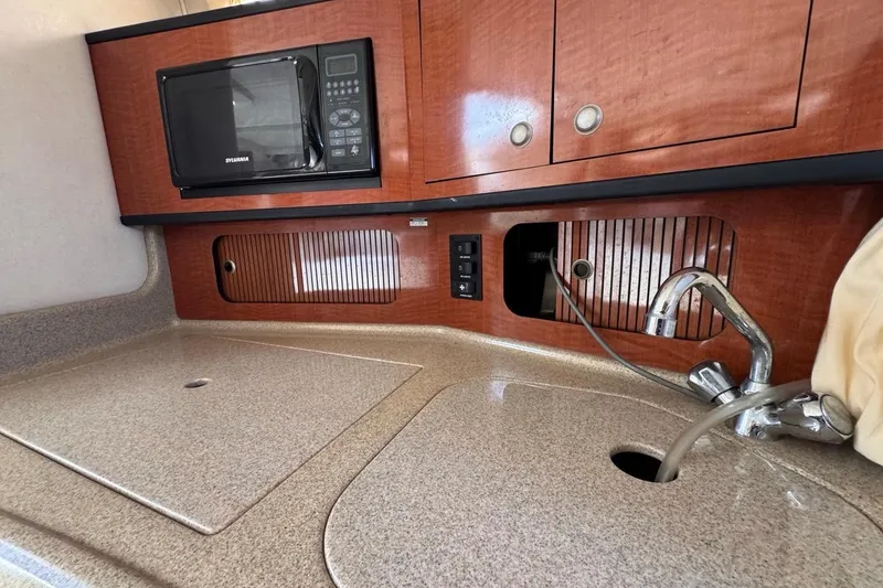 Slide: The Image of 2005 Sea Ray 300 Sundancer kitchen with microwave, sink, and wooden cabinetry. - 67