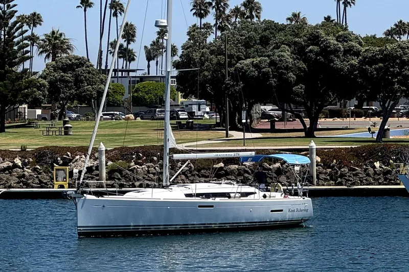 The Image of 2014 Jeanneau Sun Odyssey 379 sailboat cruising near a coastal marina. - 0
