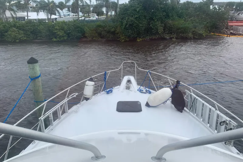 Slide: The Image of Bow view of 1999 Hatteras 52 Cockpit Motor Yacht docked near lush greenery. - 4