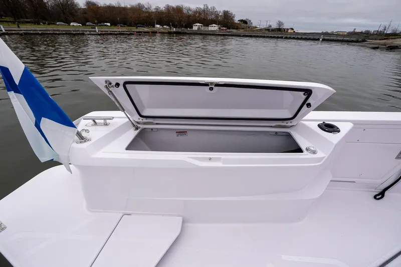 Slide: The Image of 2027 Axopar 38 Cross Cabin boat with open storage compartment and flag, docked by the water. - 19
