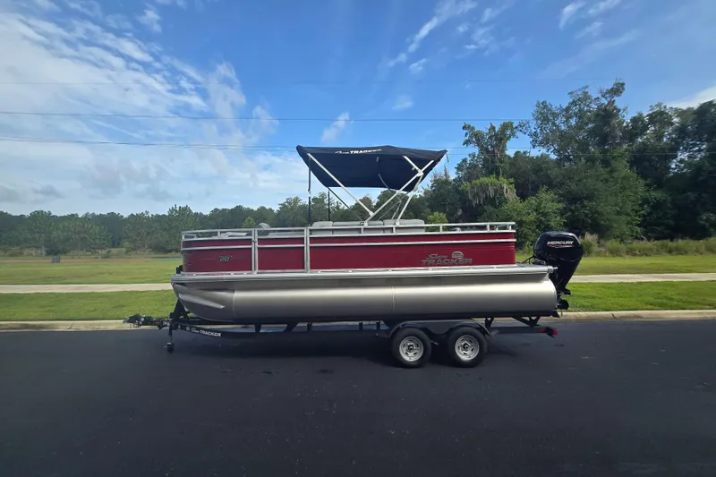 The Image of 2026 Sun Tracker SportFish 20 DLX pontoon boat on trailer, parked outdoors under blue sky. - 0
