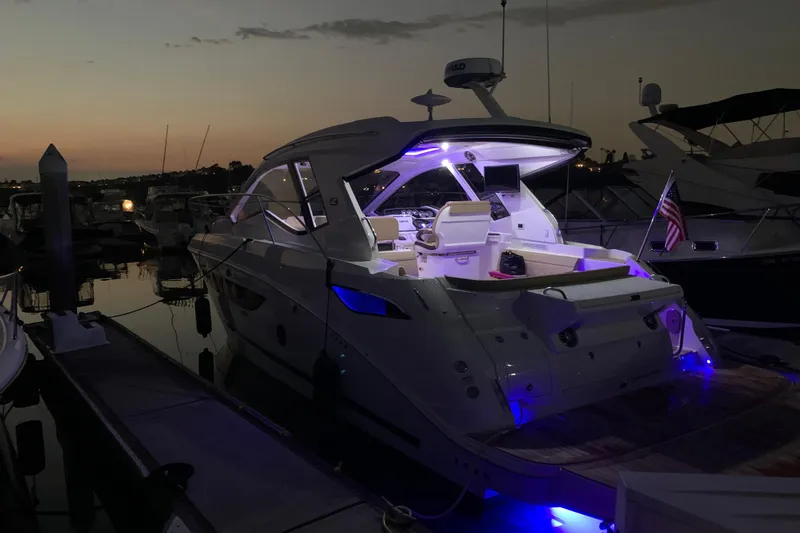 Slide: The Image of 2021 Sea Ray Sundancer 350 Coupe docked at sunset with illuminated interior and American flag. - 8