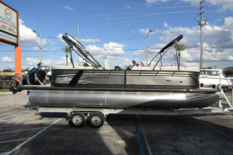 The Image of 2022 Starcraft SLS 5 pontoon boat on trailer at dealership, under clear blue sky. - 0