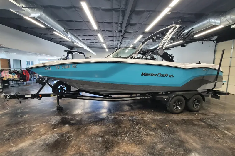 Slide: The Image of 2024 MasterCraft NXT24 boat in showroom, blue and white design, on trailer. - 12