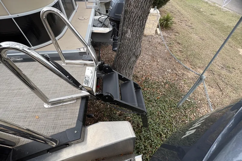 Slide: The Image of 2025 Avalon Excalibur LTD Quad Lounge boat with metal ladder and steps near a tree. - 19