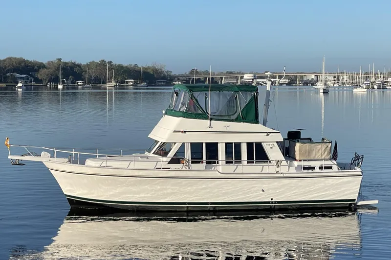 The Image of 2003 Mainship 430 Trawler on calm water, featuring green canopy and sleek design. - 0