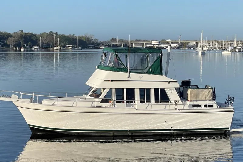 Slide: The Image of 2003 Mainship 430 Trawler on calm water, featuring green canopy and sleek design. - 2