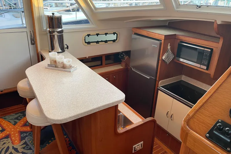 Slide: The Image of 2003 Mainship 430 Trawler kitchen with bar stools, countertop, fridge, microwave, and stove. - 24