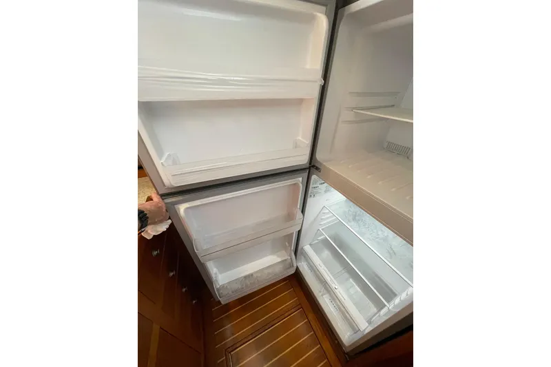 Slide: The Image of Open refrigerator inside 2003 Mainship 430 Trawler, showcasing spacious interior and wooden flooring. - 28