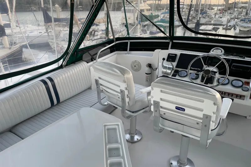 Slide: The Image of 2003 Mainship 430 Trawler helm with seating, steering wheel, and navigation equipment in marina setting. - 43