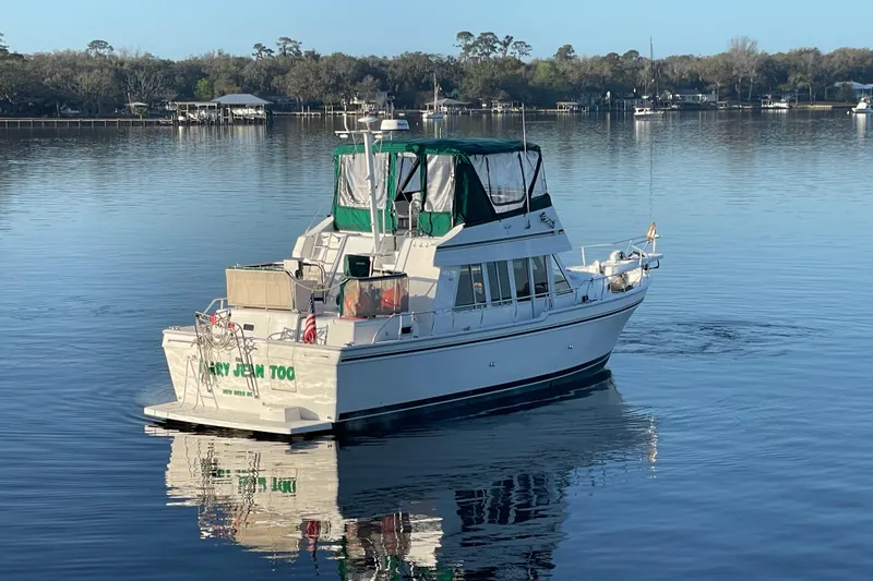 Slide: The Image of 2003 Mainship 430 Trawler on calm water, featuring green canopy and serene surroundings. - 5