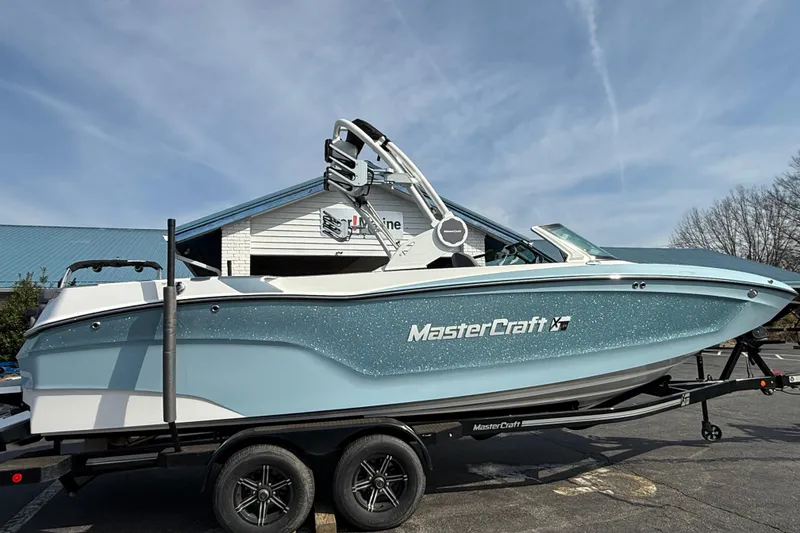 The Image of 2026 MasterCraft XT24 boat on trailer, parked outdoors under clear sky. - 0