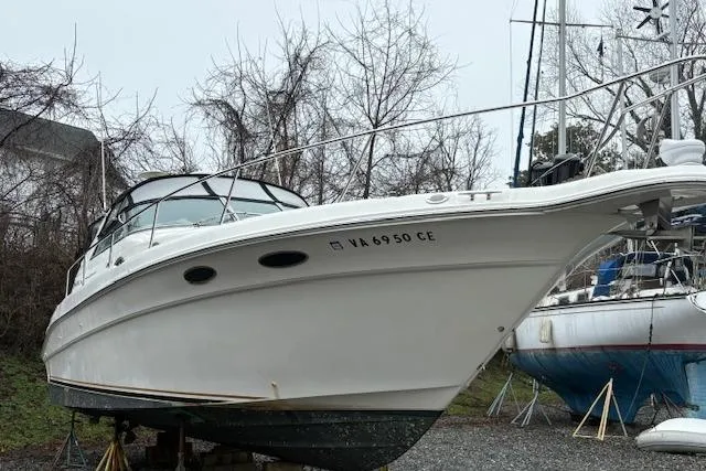 The Image of 1998 Sea Ray Sundancer 330 boat on land, white hull, parked near other boats. - 0