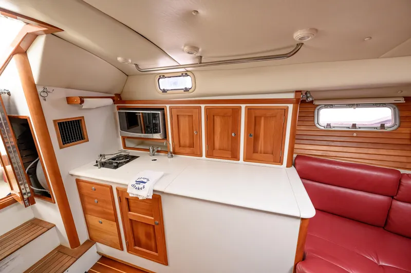 Slide: The Image of 2005 MJM 34z Downeast yacht interior with wooden cabinets, kitchenette, and red seating. - 18