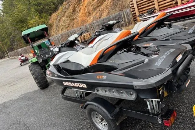 Slide: The Image of 2013 Sea-Doo GTI SE 130 jet skis on trailer, parked near a green tractor. - 2