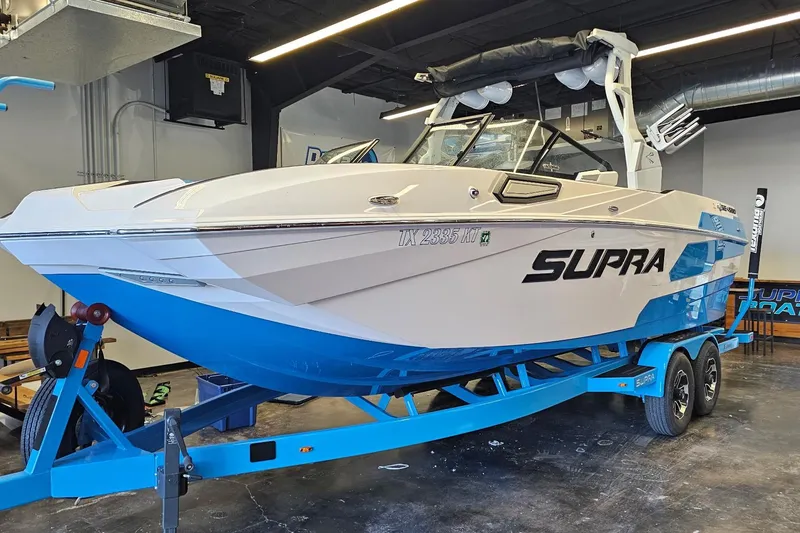 The Image of 2023 Supra SE 550 boat on blue trailer in showroom. - 2