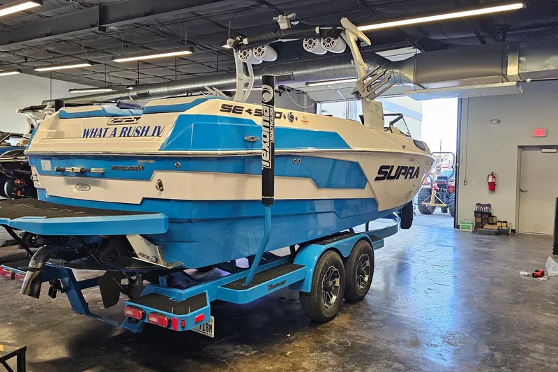 Slide: The Image of 2023 Supra SE 550 boat in a garage, blue and white design on trailer. - 7