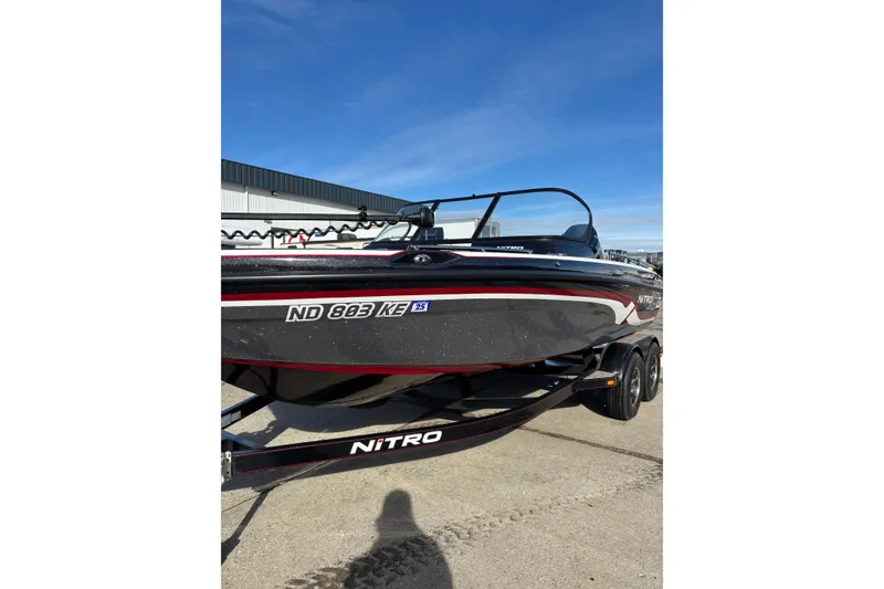 The Image of 2015 Nitro ZV18 boat on trailer, black with red accents, parked outdoors. - 1