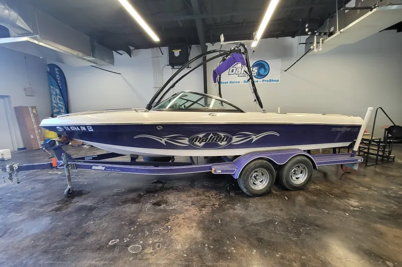 Slide: The Image of 2003 Malibu Sunsetter LXi boat on trailer in showroom, featuring sleek design and purple accents. - 5
