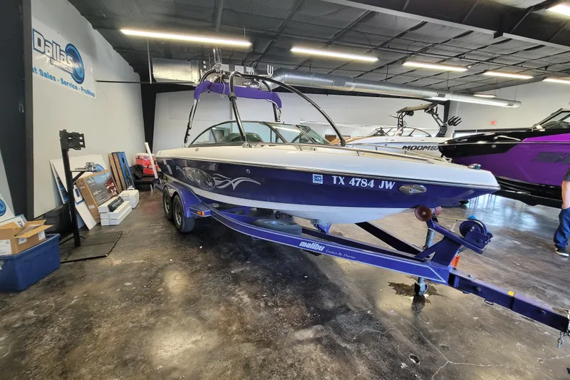 Slide: The Image of 2003 Malibu Sunsetter LXi boat on trailer in showroom, featuring sleek design and graphics. - 7