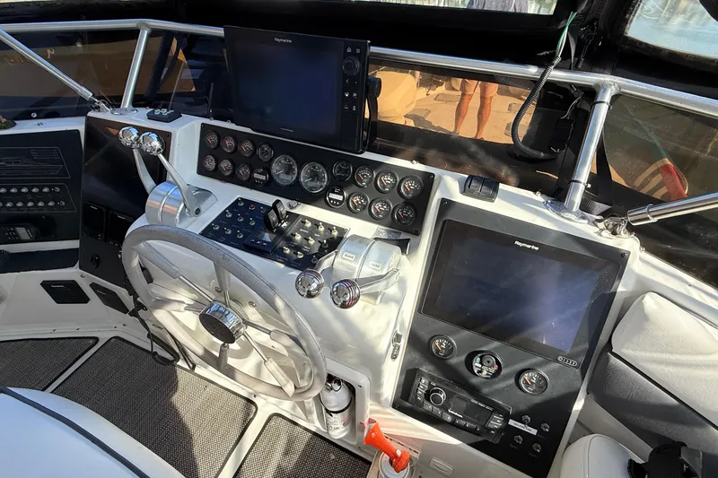 Slide: The Image of 1998 Mainship 47 Motor Yacht helm with steering wheel, gauges, and navigation screens. - 14