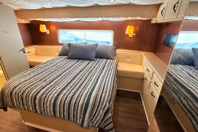 Slide: The Image of 1998 Mainship 47 Motor Yacht bedroom with striped bedding, cozy seating, and warm lighting. - 41