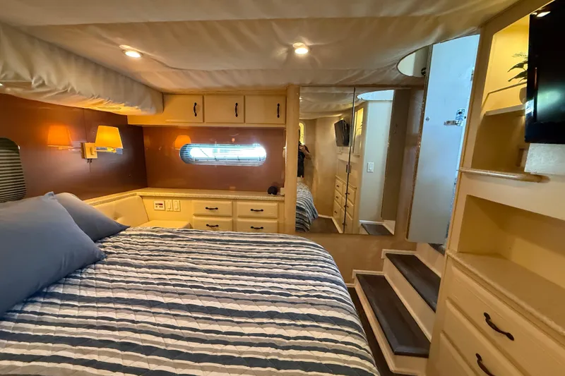 Slide: The Image of Cozy bedroom in 1998 Mainship 47 Motor Yacht with striped bedding and warm lighting. - 48