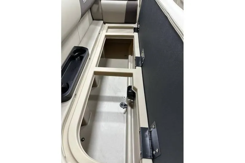 Slide: The Image of 2026 Bennington 21 SSR Quad Bench storage compartment, open with beige interior and cup holders. - 14